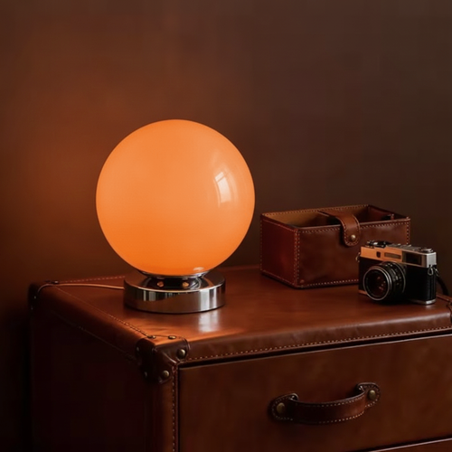 Lampe à poser boule en verre orange allumée sur une commode