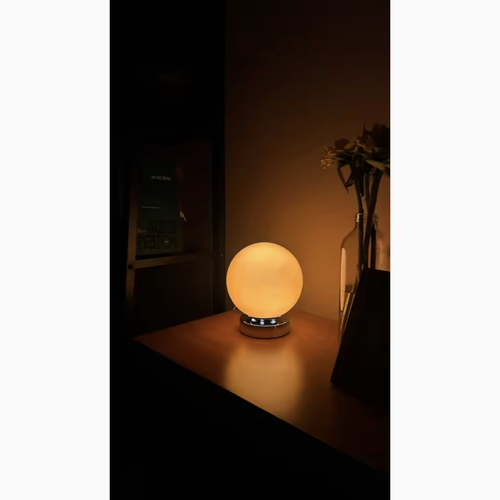 Lampe à poser boule en verre orange allumée le soir, photo client