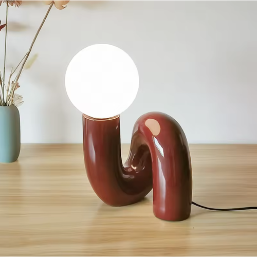 Lampe à poser boule en verre, pied ondulé bordeaux allumée sur un bureau
